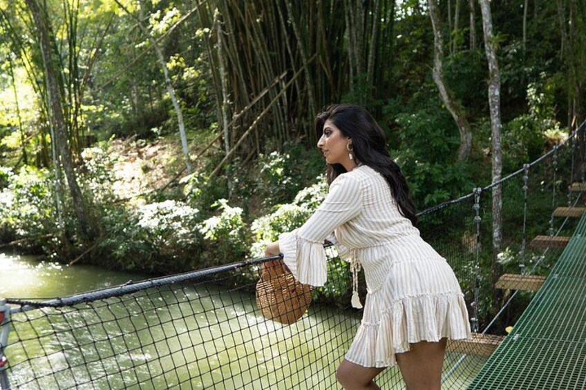 A person standing on a rope bridge over a river, surrounded by greenery. 2