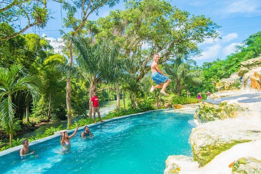 A person jumping into a pool surrounded by lush greenery and rocky terrain. 3