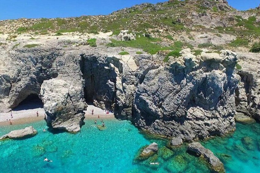 Une côte rocheuse bordée d’eaux turquoise et limpides, une petite formation rocheuse ressemblant à une grotte, et une colline lointaine à la végétation clairsemée. 2