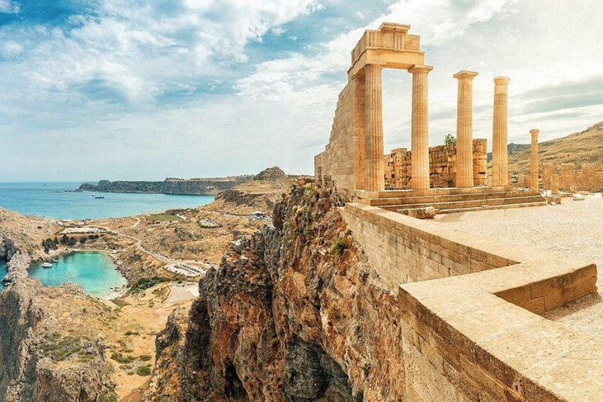 Ancient ruins with columns, a rocky coastline, and a small body of water. 1