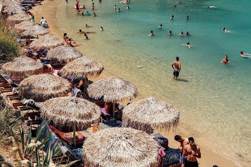 Una playa con sombrillas de paja, gente nadando y tomadores de sol. 2