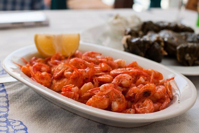 A plate of cooked shrimp with lemon wedges on a table. 4