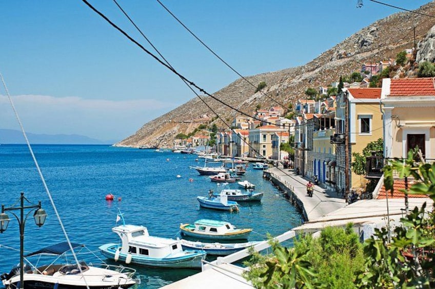 A coastal town with boats docked along the waterfront, buildings with red-tiled roofs, and a hilly landscape in the background. 3