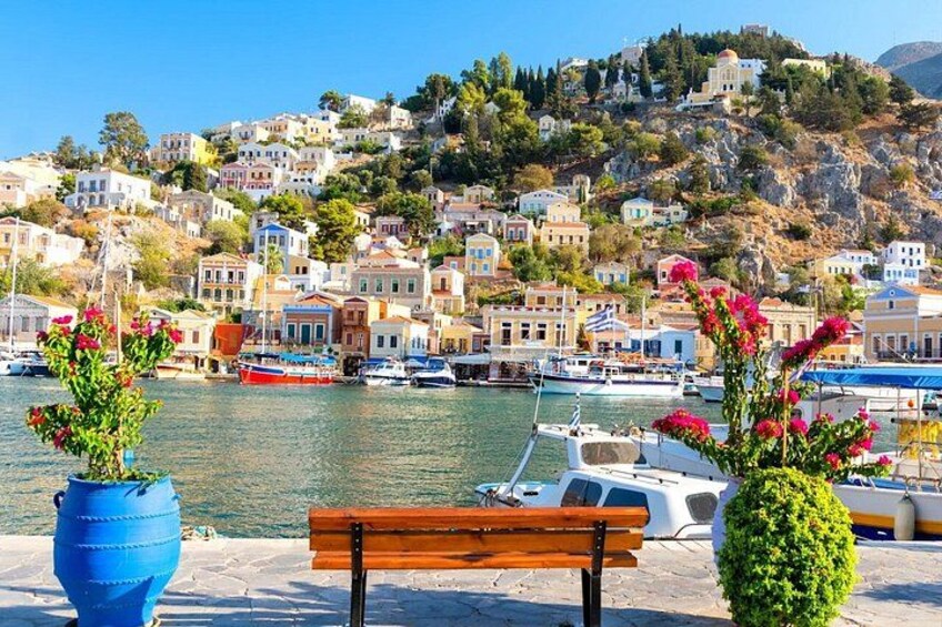 A coastal town with colorful buildings, a wooden bench, and a blue planter with flowers. 1