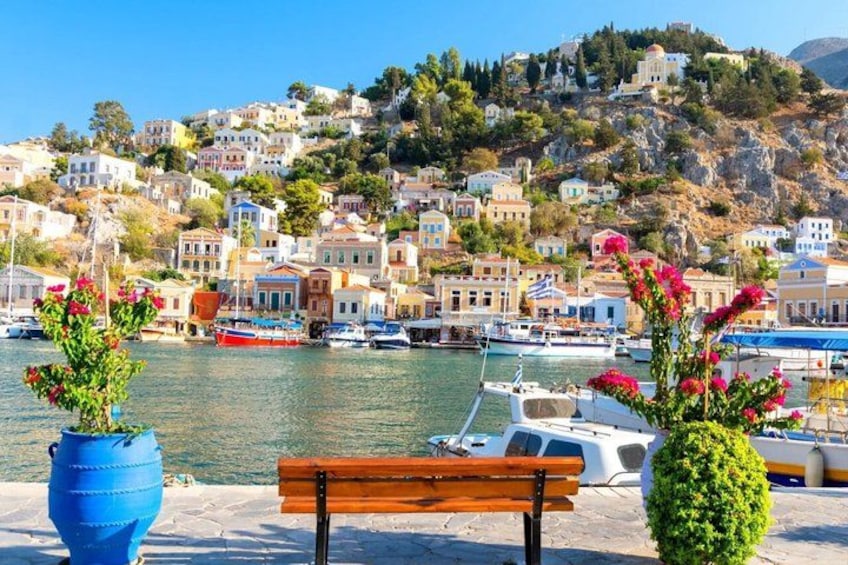 A coastal town with colorful buildings, a wooden bench, and a blue planter with flowers. 1