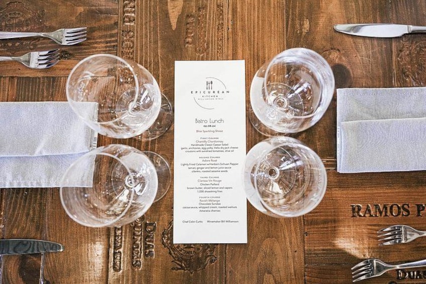 A wooden table with a menu, wine glasses, and cutlery. 2