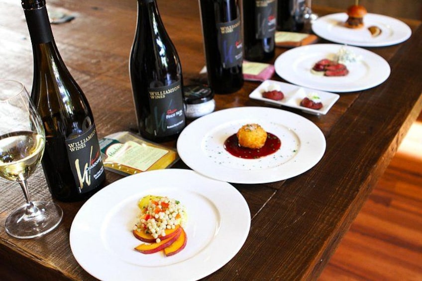 A wooden table with wine bottles, glasses, and plates of food. 1