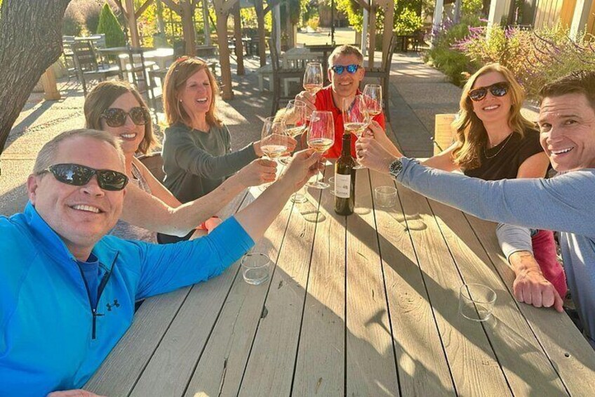Un groupe de personnes trinquant avec des verres de vin autour d’une table en bois, à l’extérieur. 2
