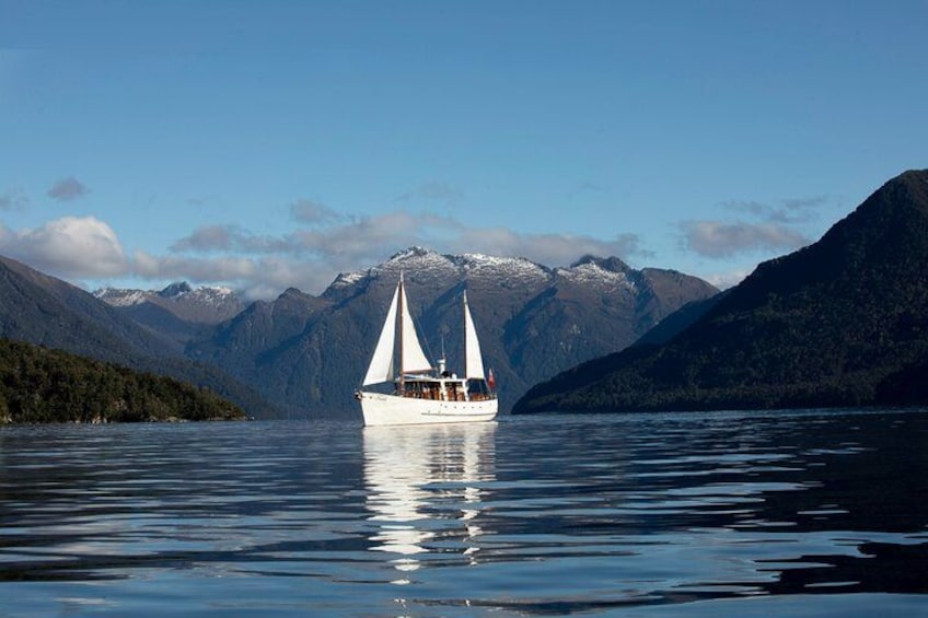 A sailboat on calm waters with mountains in the background. 1