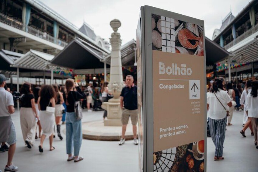 Een levendig winkelgebied met een bordje 'Bolhão' en een fontein op de achtergrond. 2