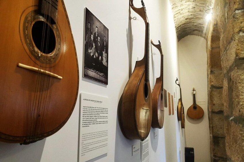 Un mur orné de plusieurs instruments de musique à cordes, dont un luth et une guitare, ainsi que de panneaux explicatifs et d’une photographie en noir et blanc. 4