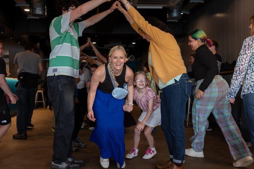 People dancing in a room with wooden floors and chairs. 5