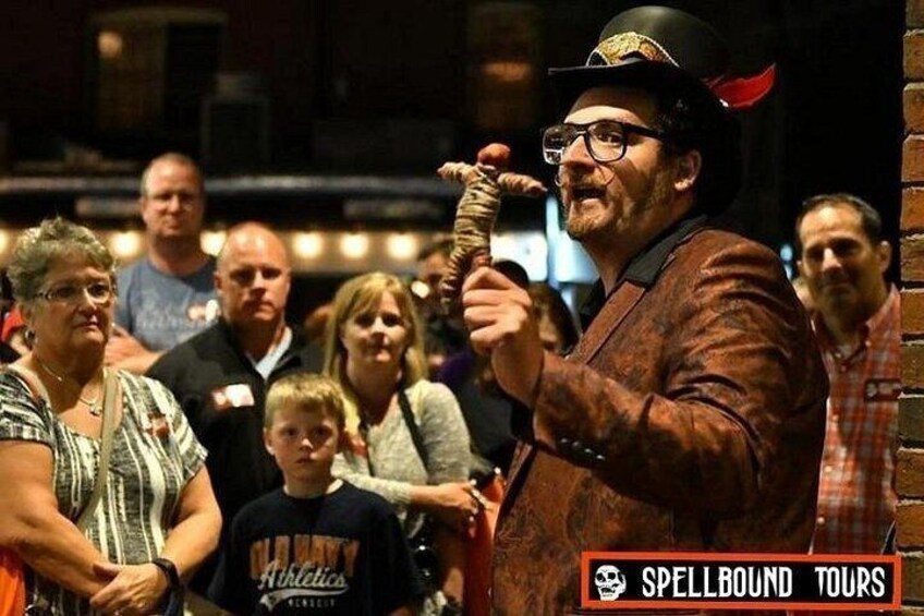 A man in a brown jacket and hat holding a sword, surrounded by a crowd. 5