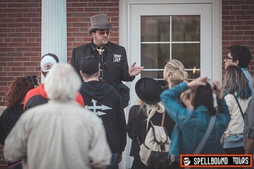 A group of people gathered outside a building with a brick facade and a white door. 3