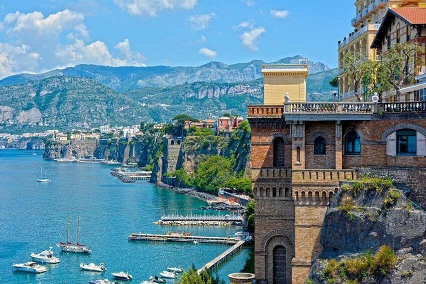 Un pueblo costero con un edificio histórico, un puerto deportivo con barcos y montañas al fondo. 5
