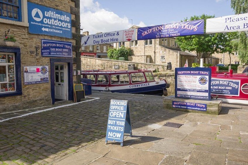 A boat trip booking office, a sign for booking tickets, and a boat docked at the pier. 2