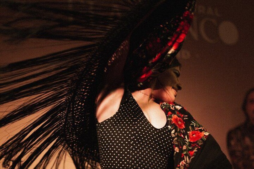 Una persona con un vestido de lunares negros y un chal con motivos florales. 1
