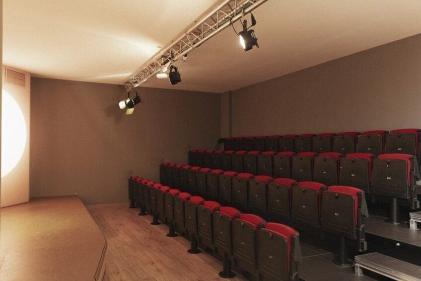 A theater with rows of red seats and a stage. 2