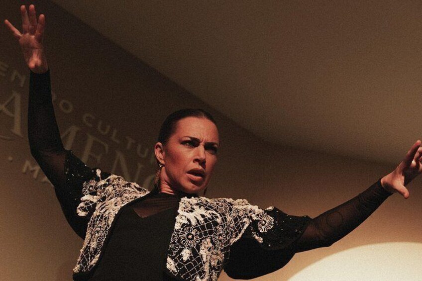 A person in a black outfit with intricate white patterns, performing with arms raised. 4