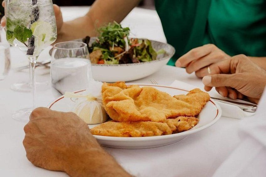 A plate of breaded cutlets, a glass of water, and a salad on a table. 4