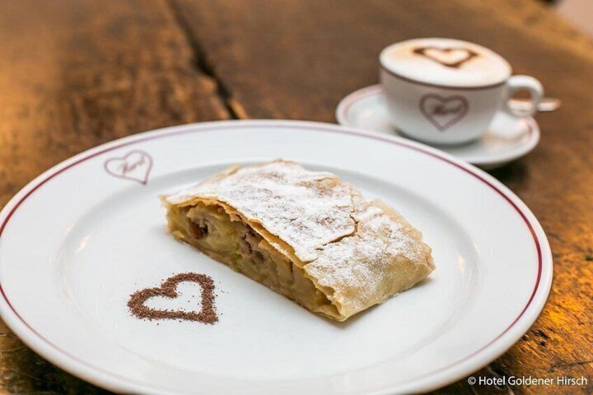 Una porción de strudel de manzana en un plato con diseño de corazón, una taza de café con diseño de corazón y una mesa de madera. 3
