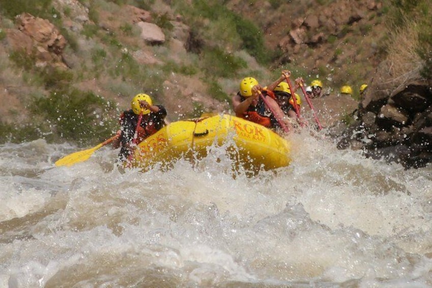 A group of people in a yellow raft navigating a river rapids. 5