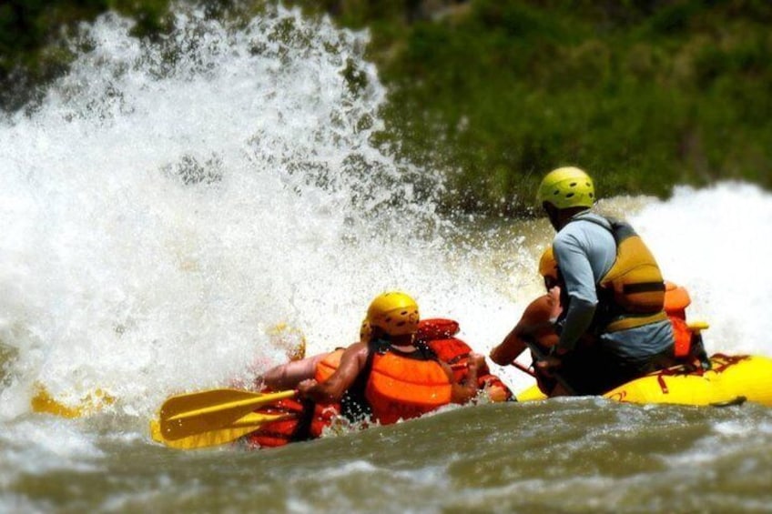 Two people in a yellow kayak navigating a river with white water. 1