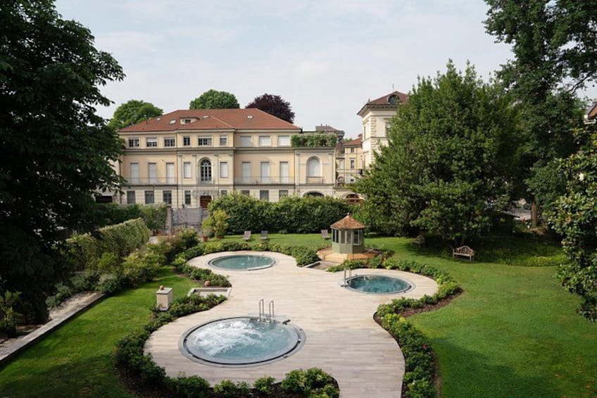 A landscaped garden with two circular pools, a gazebo, and a large building in the background. 2