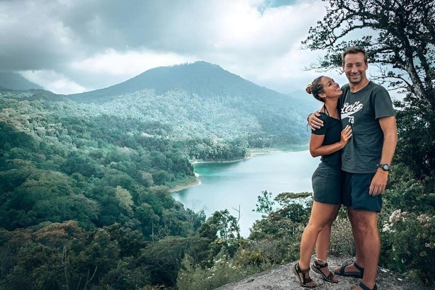 A couple standing on a mountain overlooking a lake surrounded by dense forest. 2