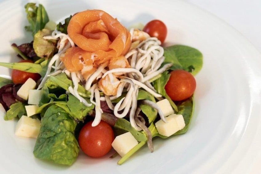 A salad with leafy greens, cherry tomatoes, cheese, and salmon. 2
