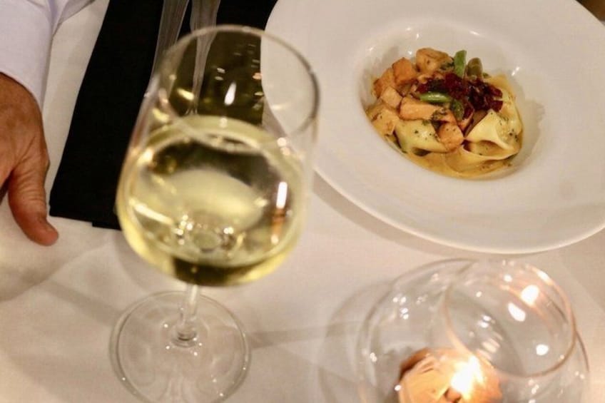 A person holding a wine glass, a plate of food, and a lit candle on a table. 3