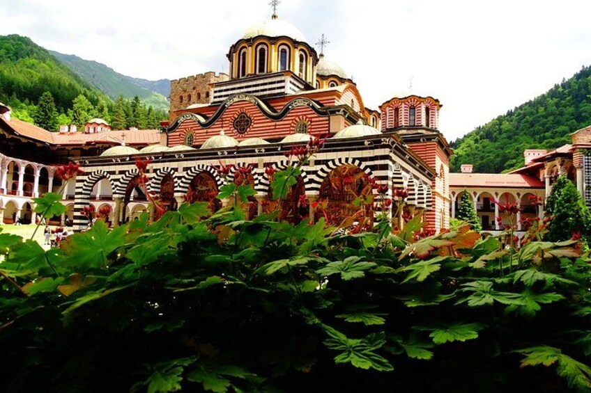 A historic church with a red and white facade, surrounded by lush greenery and mountains in the background. 4