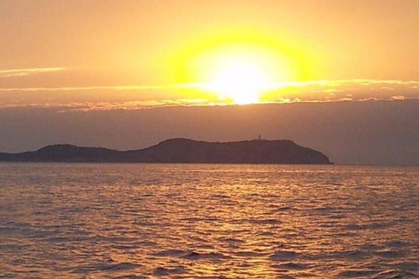 Un coucher de soleil sur une étendue d’eau, avec la silhouette d’une masse terrestre visible au loin. 1