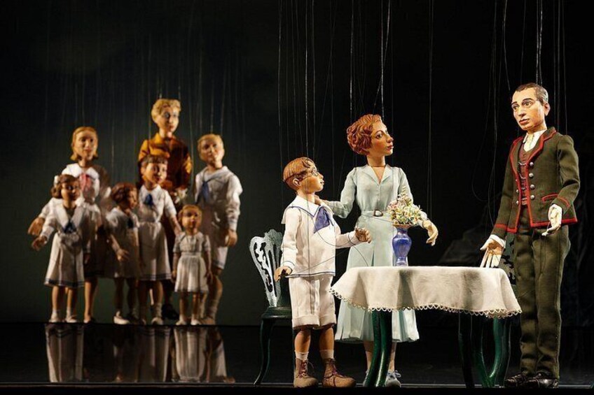 A puppet theater with figures on stage, a table, and a puppet master. 3