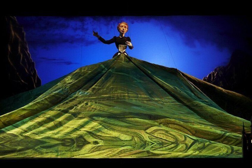 A person in a green dress standing on a mountain peak with a blue sky in the background. 2