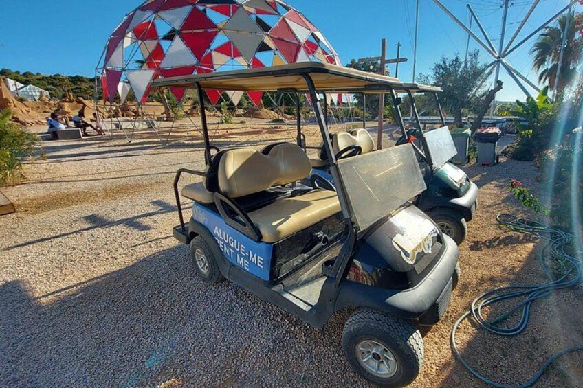 A golf cart with 'ALUGUE-ME' written on it, parked on a gravel surface. 3