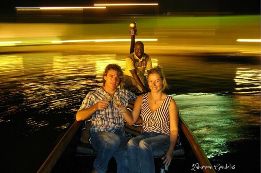 Three people in a boat on a body of water with reflections of lights. 2