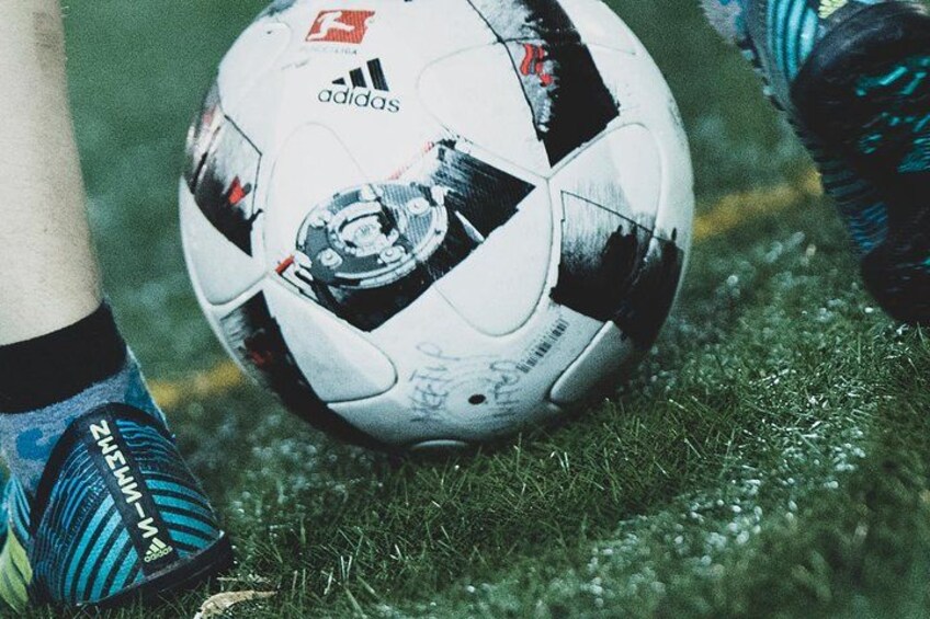 A soccer ball on a grassy field with a person's leg and shoe in the foreground. 1