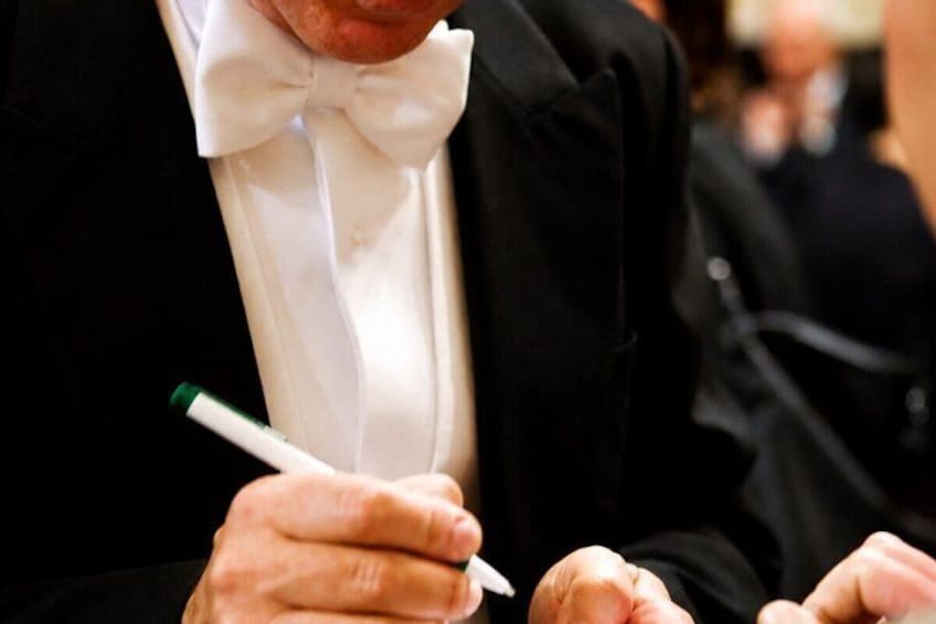 Eine Person in einem schwarzen Anzug und weißem Hemd mit Fliege, die einen Stift hält. 2
