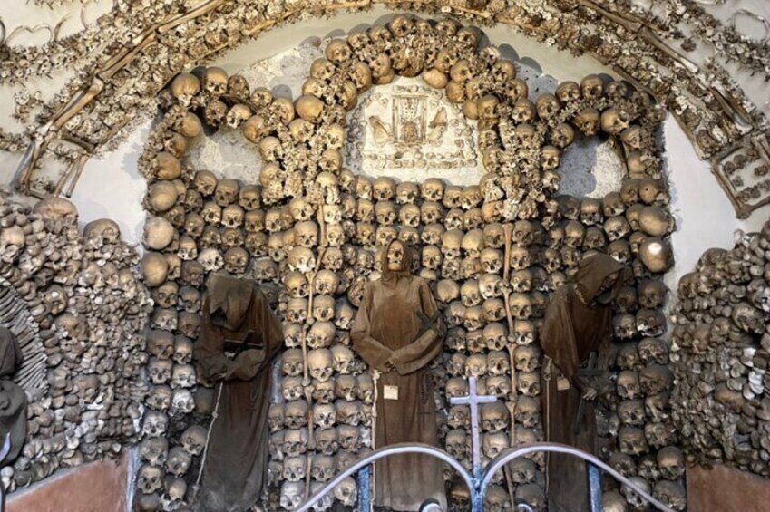 A mausoleum with numerous skulls arranged in patterns and three statues. 1