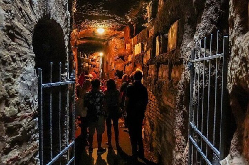 A narrow passageway with stone walls and metal gates, illuminated by a single light source at the end. 3