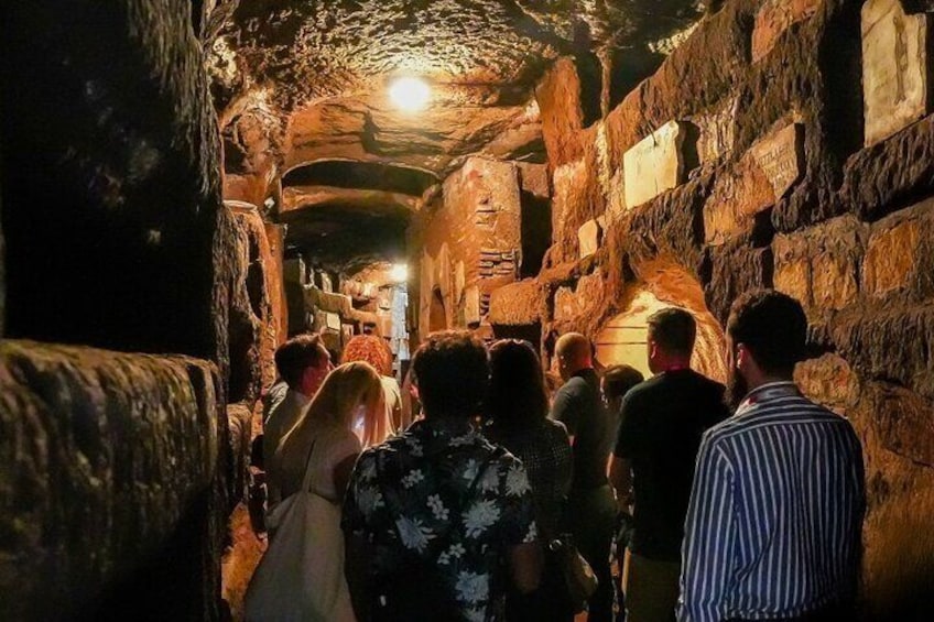 A group of people walking through a narrow, stone-walled passageway with a light at the end. 4