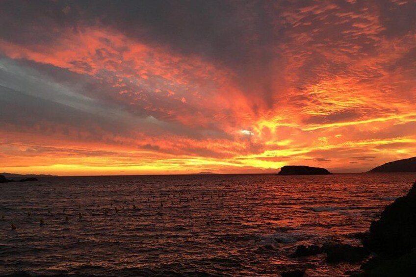 A sunset over a body of water with a rocky coastline. 2