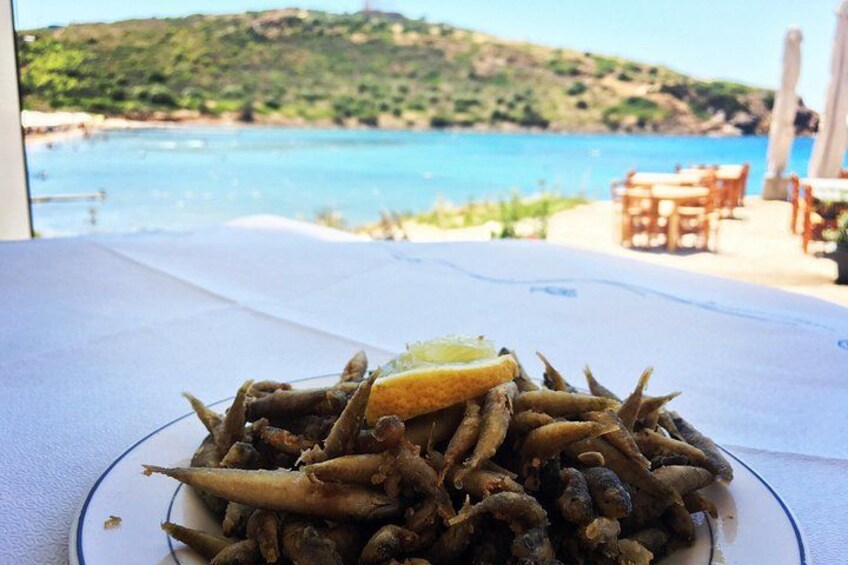 A plate of fried fish with lemon on a table with a view of a beach and mountains. 3