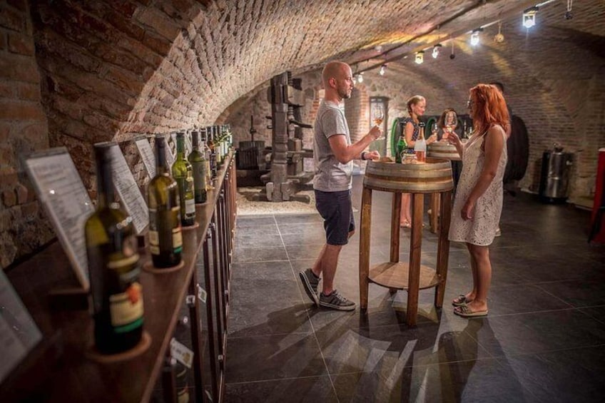 Une cave à vin avec un mur en briques, une longue table couverte de bouteilles de vin et des personnes en train de déguster du vin. 2