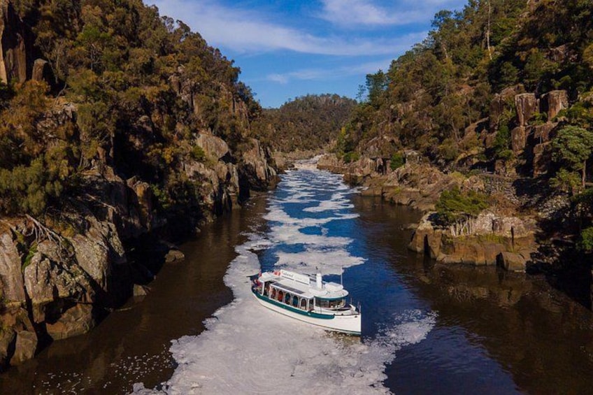 A boat navigating a narrow river surrounded by rocky cliffs and dense vegetation. 3