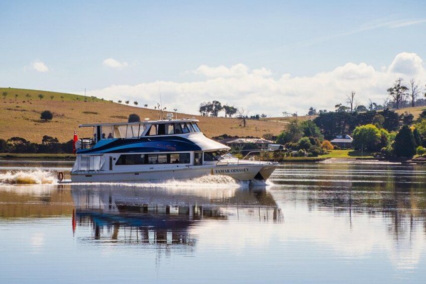 A boat named 'Tamarind' on a calm river with a clear sky and a hilly landscape in the background. 1