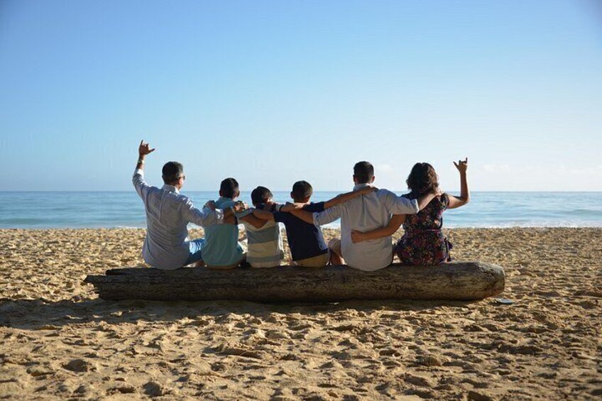 A group of people sitting on a log on a sandy beach with the ocean in the background. 3