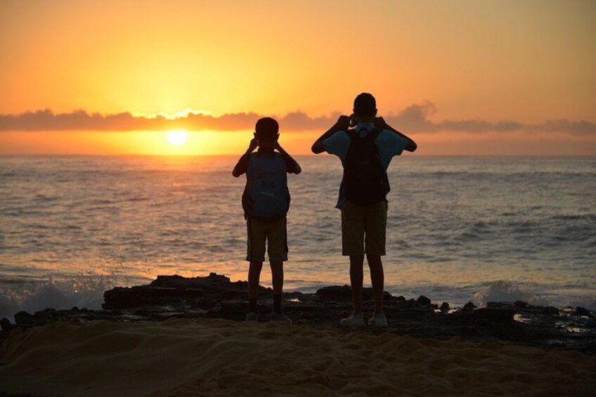 Zwei Personen stehen an einem Strand bei Sonnenuntergang und blicken auf den Ozean. 3