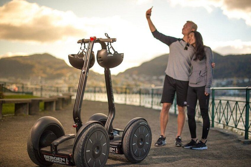 A person taking a selfie with a Segway, a body of water, and mountains in the background. 2